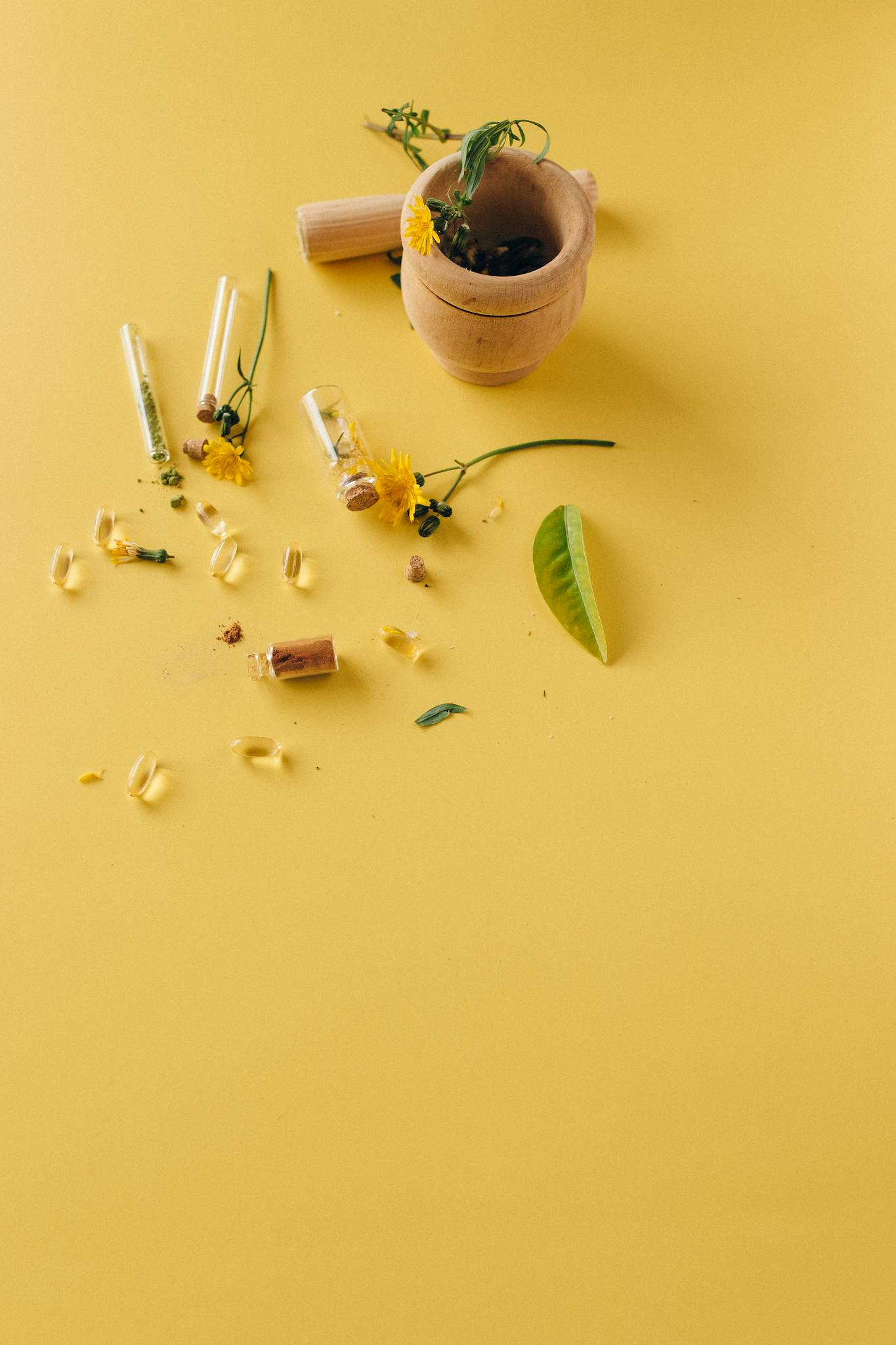Natural herbal supplements and remedies displayed with a mortar and pestle on a vibrant yellow surface.